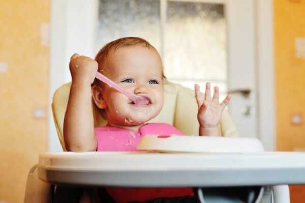 baby in high chair being fed peanut butter in cereal as peanut allergy prevention